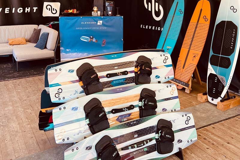 Eleveight Kiteboards im Zelt aufgereiht im Boardständer auf Holzboden in großem Zelt am Strand