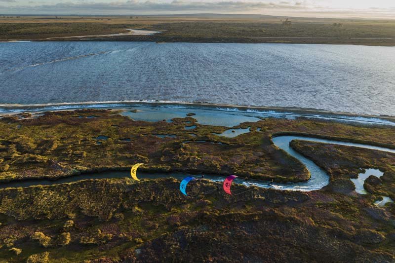 North Kiteboarding - drei Kitesurfer kiten in einem kleinen Seitenarm direkt am Meer oder einer Flussmündung und es ist viel Grün drum herum